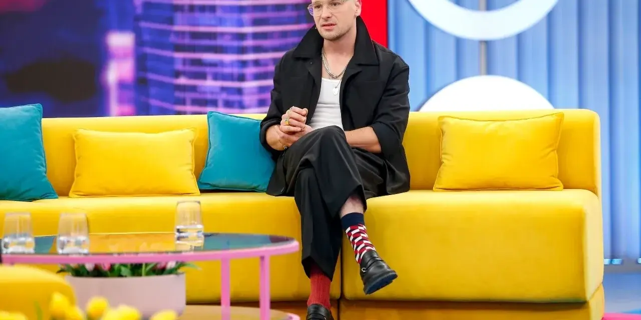 Krzysztof Zalewski w czarnym garniturze siedzi na żółtej kanapie, jakby przygotowywał się do nagrania jednego z jego filmów.