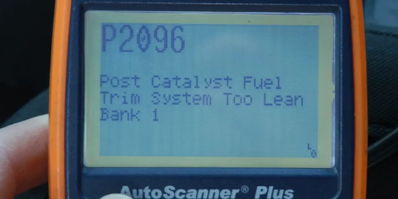An orange and blue Actron AutoScanner Plus displays error code P2096: Post Catalyst Fuel Trim System Too Lean Bank 1.