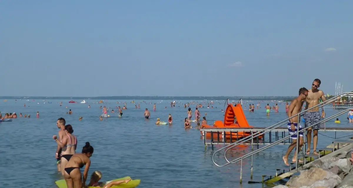 Tłum ludzi cieszy się słońcem i wodą. Dzieci bawią się na dmuchanej zjeżdżalni, a dorośli pływają i relaksują się. Wszyscy zasila Balaton w gorący letni dzień.