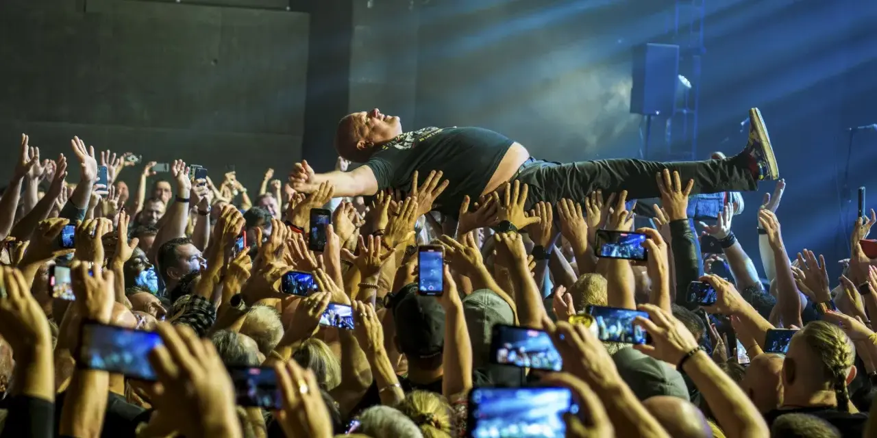 Kult w Arahji: wokalista zespołu niesiony przez tłum, fani nagrywają koncert telefonami.