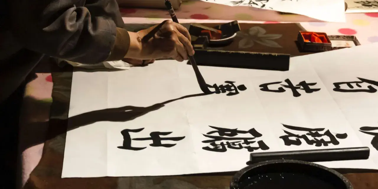 Une main manie un pinceau pour créer de la calligraphie chinoise sur du papier blanc. Des caractères noirs se déploient, témoins d'un art ancestral.