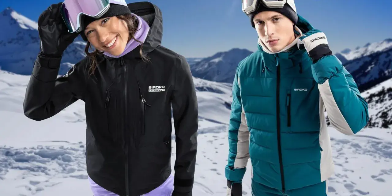 Coppia con abbigliamento da sci, giacche hardshell e maschere da neve, su sfondo montuoso innevato.