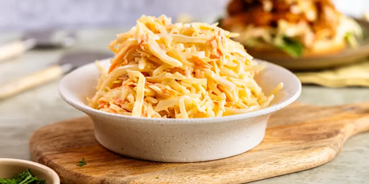 Schüssel mit cremigem Krautsalat, perfekt für ein **Rezept Coleslaw original**. Im Hintergrund ein Burger.