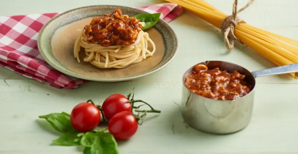 Pyszny sos do spaghetti z mięsem mielonym, podany na talerzu z makaronem, obok świeżych pomidorków i bazylii.
