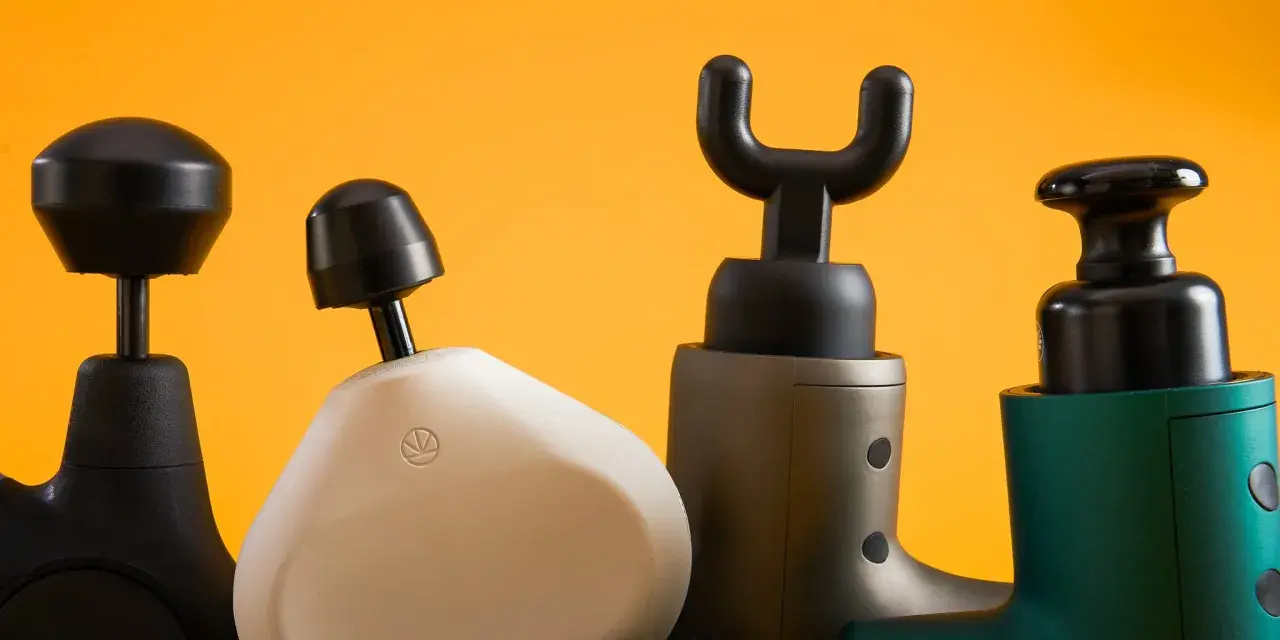 Four percussion massagers with different attachments are lined up against a bright orange background.
