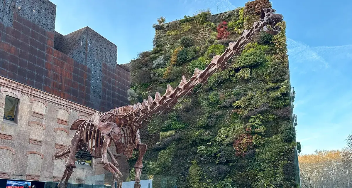 Szkielet dinozaura przed zieloną ścianą budynku. Madryt nietypowe atrakcje, które zaskakują.