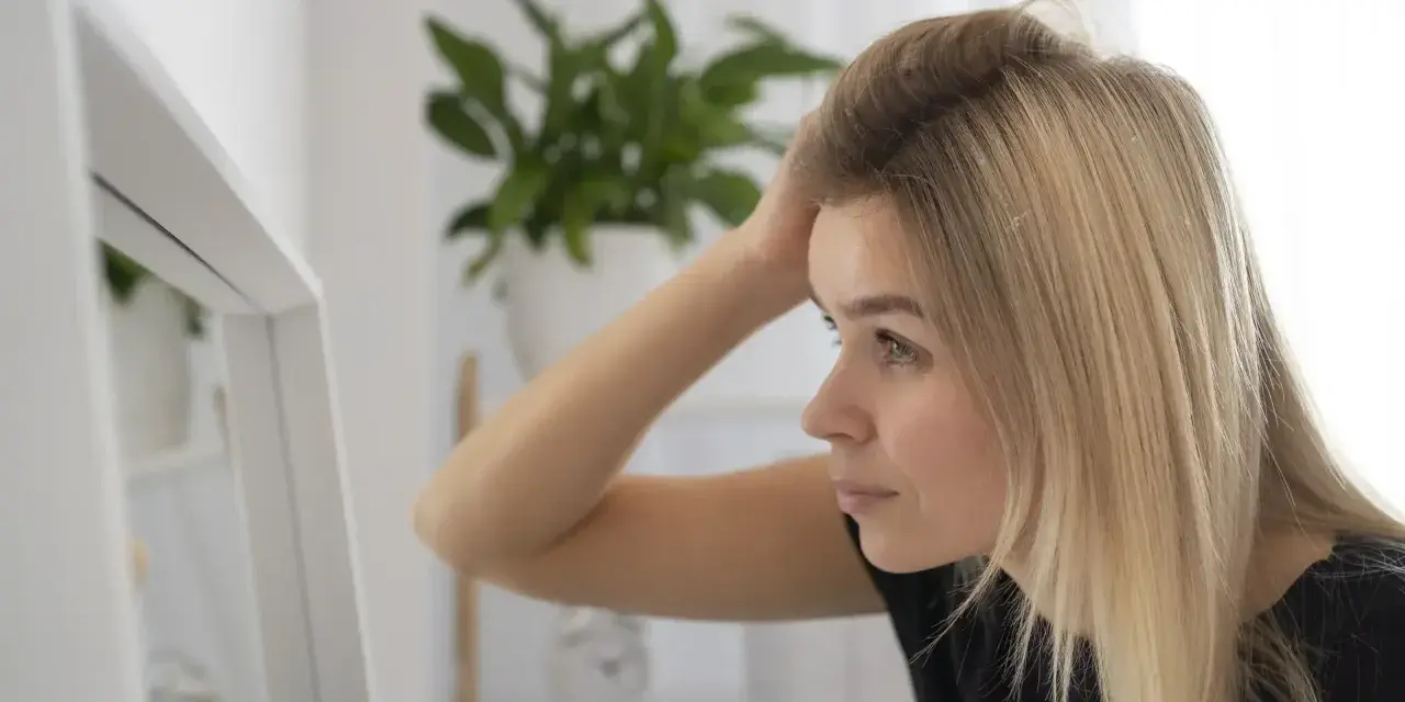 Kobieta z blond włosami sprawdza w lustrze, czy jej włosy są czyste po umyciu szamponem z **ammonium lauryl sulfate**.