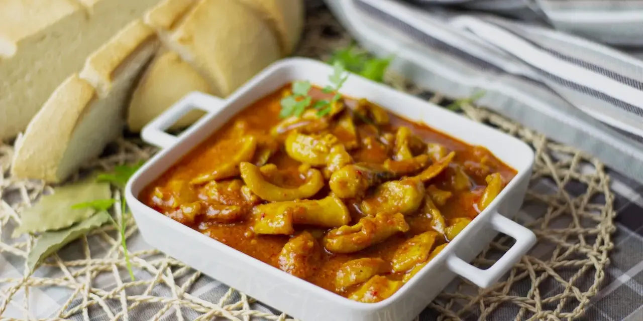 Delicioso plato de sepia en salsa, servido en cazuela blanca, acompañado de pan rústico y hojas de laurel.