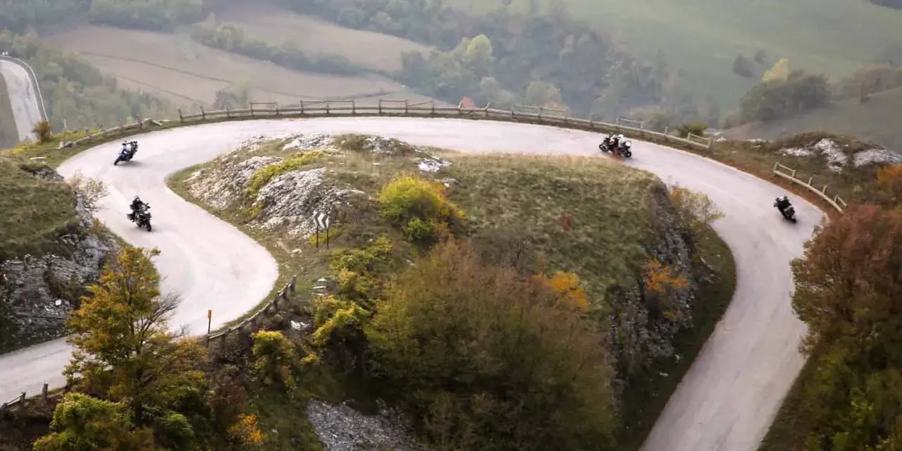Motociclisti sfrecciano sulle curve delle Gole del Furlo, immersi in un paesaggio autunnale.