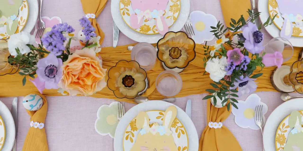 Jolie table de Pâques avec des lapins en papier, des fleurs fraîches et des œufs décorés. Une belle idée déco table Pâques pour un repas printanier.