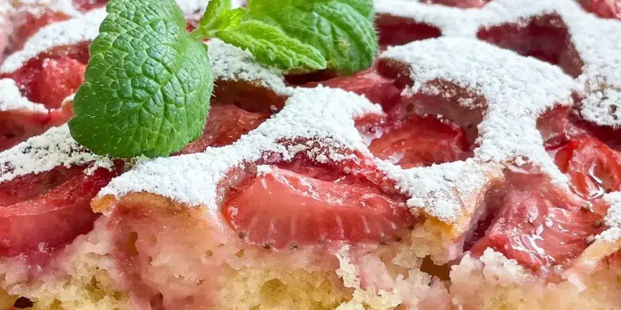 Szybkie ciasto z truskawkami, posypane cukrem pudrem i ozdobione listkiem mięty. Idealne na letnie popołudnie.