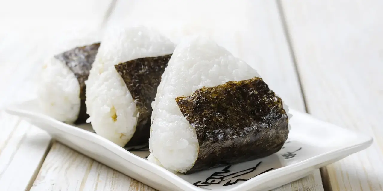 Trzy ryżowe kulki onigiri z nori na białym talerzyku. Idealne na szybki lunch, oto prosty onigiri przepis.