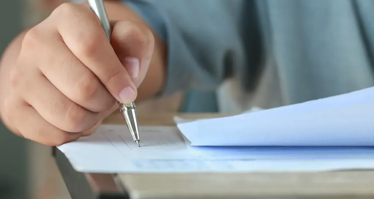 Dłoń trzymająca długopis, która wypełnia test. Czy przed jak również stawiamy przecinek, gdy piszemy.