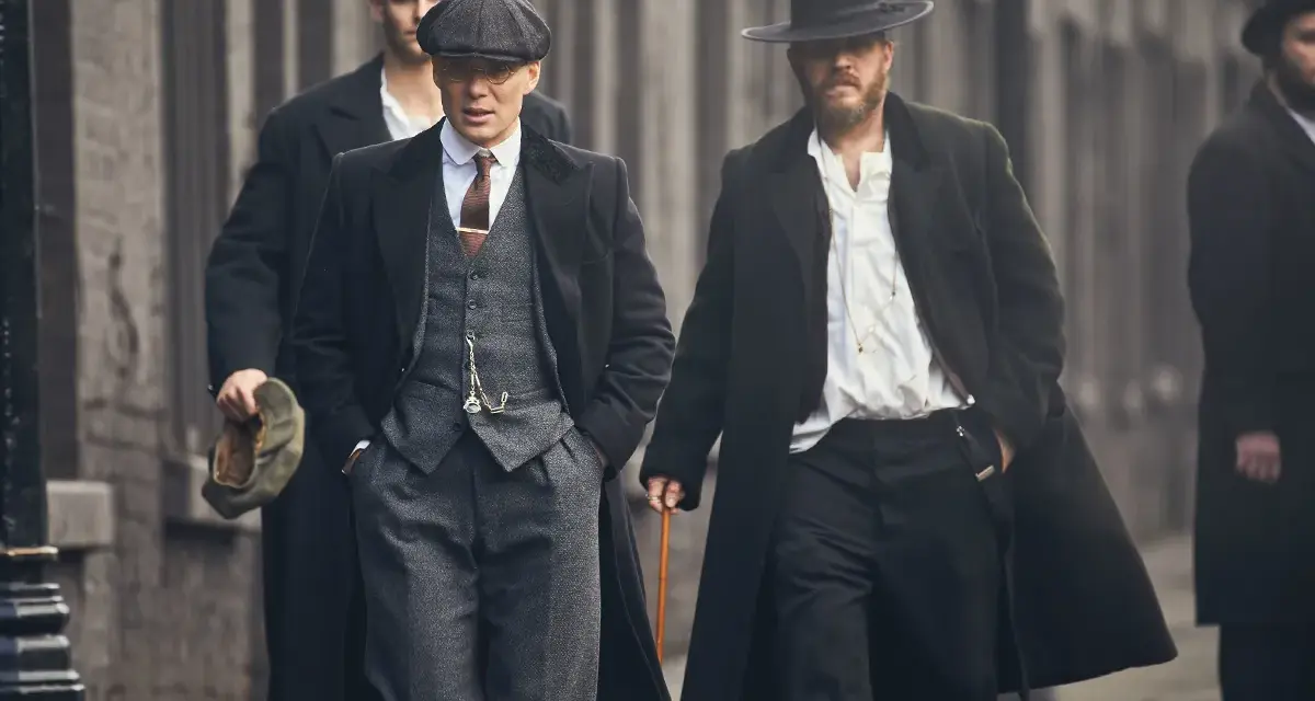 Tommy Shelby e altri uomini in abiti eleganti camminano per strada.