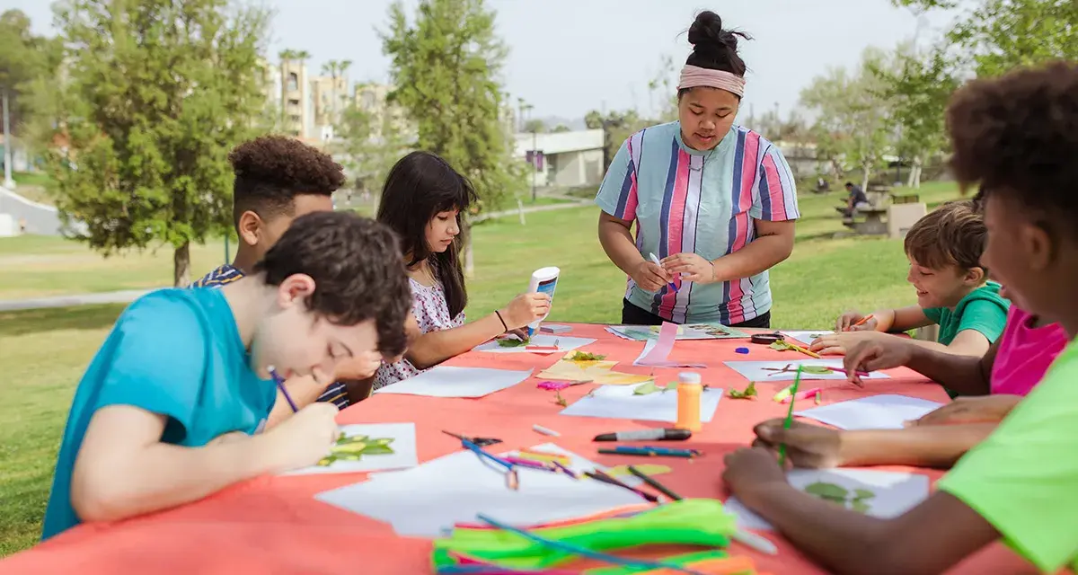 Des enfants créatifs participent à un atelier d'art en plein air, une activité typique d'un centre de loisirs ou d'un camp d'été, peut-être dans le cadre d'un programme ACM BAFA.