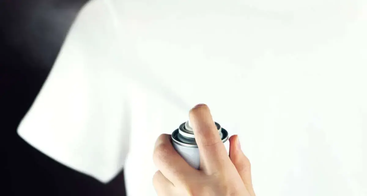 Hand sprüht mit einer Dose auf ein weißes T-Shirt, um statische Aufladung zu verhindern.