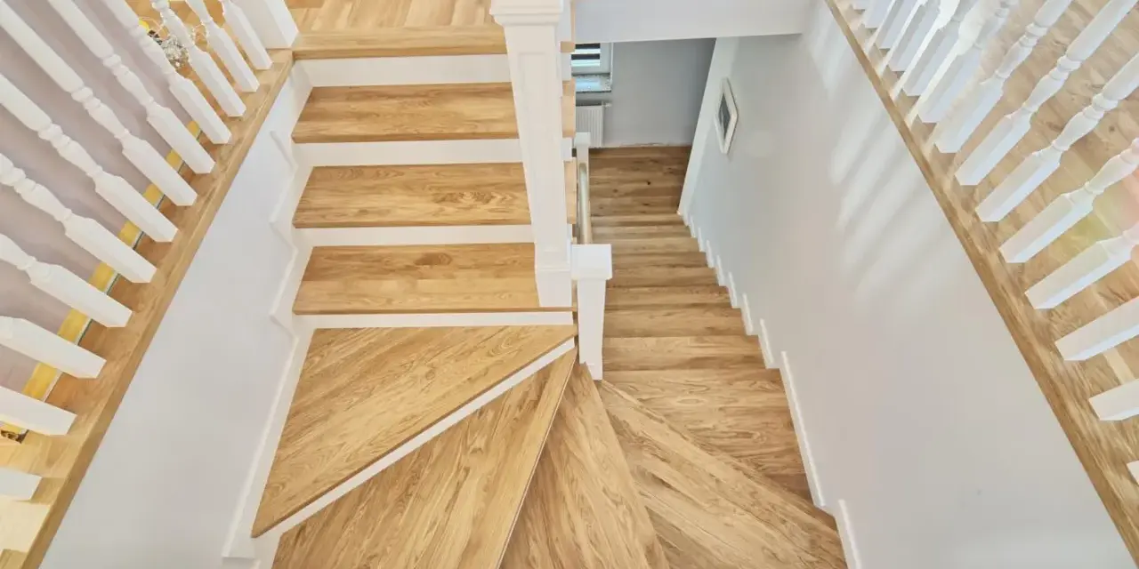 Eleganckie schody angielskie z drewna dębowego, z białymi balustradami, prowadzą w dół.
