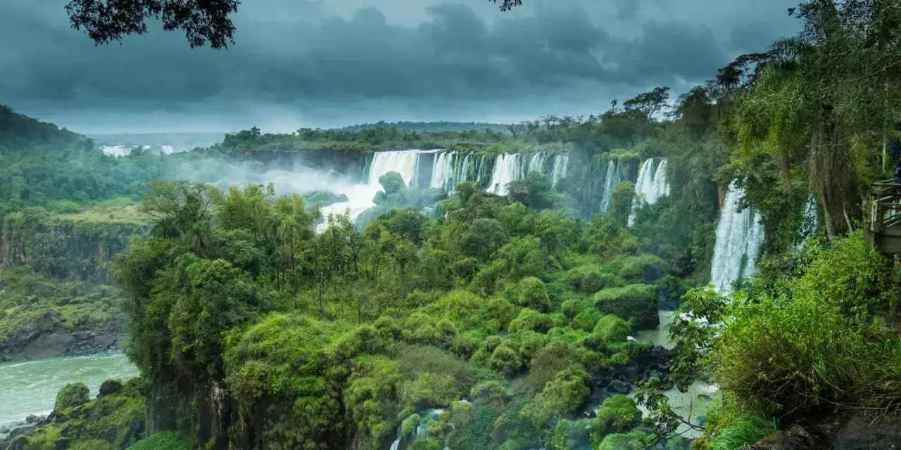 Majestuosas cataratas del Iguazú, un torrente de agua cayendo entre exuberante vegetación bajo un cielo nublado.