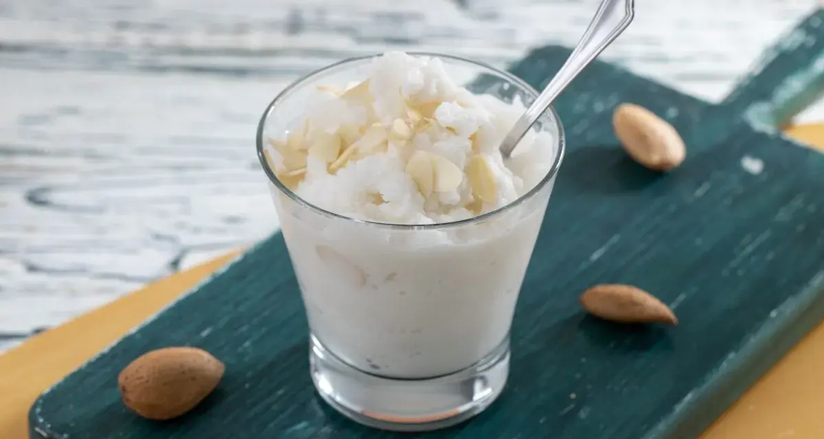 Rinfrescante granita alla mandorla, guarnita con lamelle di mandorle, servita in un bicchiere su un tagliere scuro.