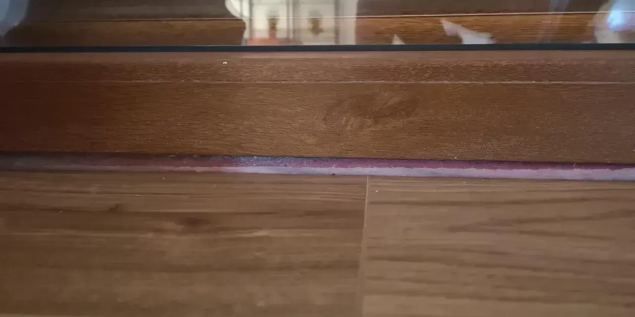 Widoczna dylatacja paneli w drzwiach, drewniana podłoga i rama okna.