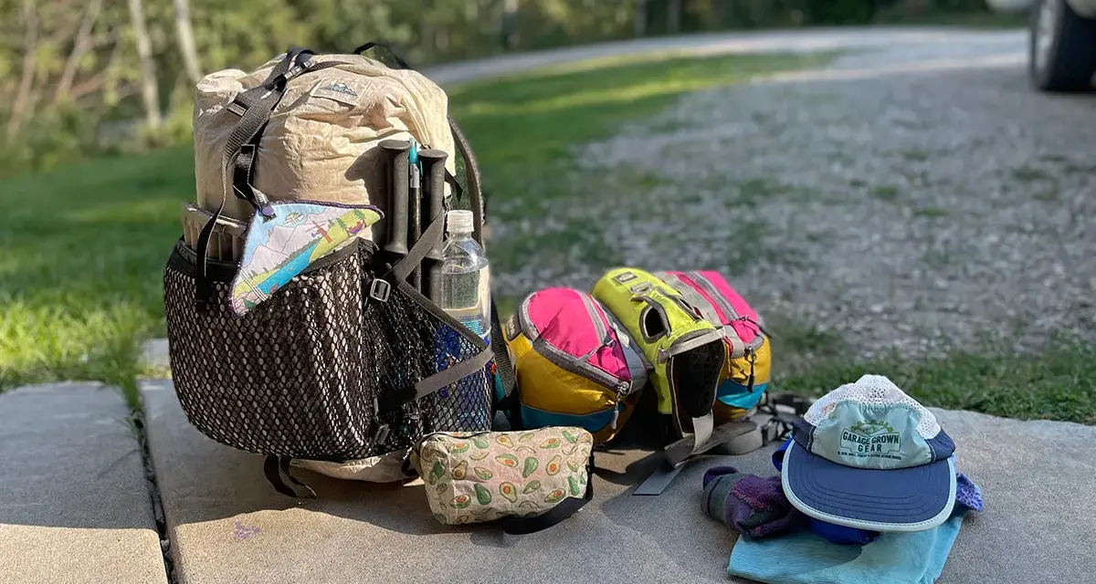 Backpack, water bottle, hiking poles, and colorful pouches are laid out, ready for a trip. This is how to pack light for an adventure.