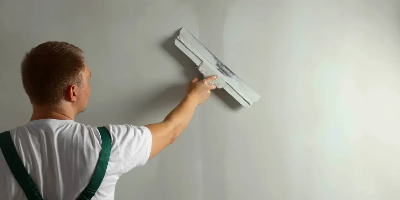 Pracownik nakłada tynk na ścianę. Czas schnięcia tynku zależy od warunków.