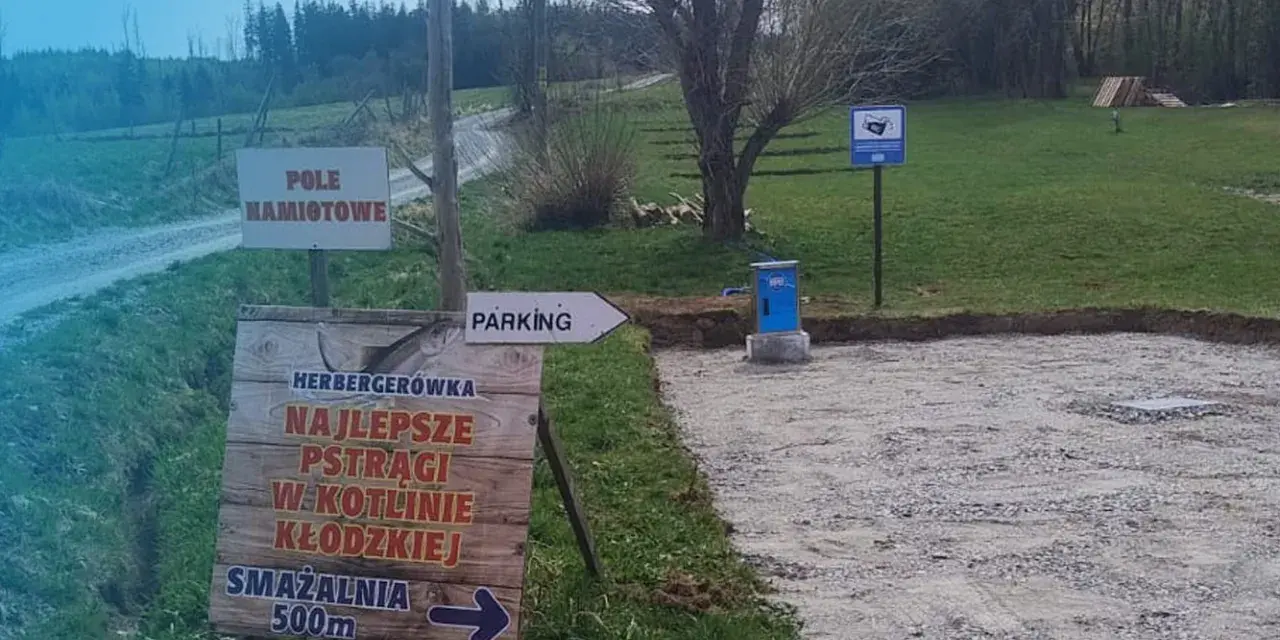 Miejsce na parking dla kamperów. Obok znak "Pole Namiotowe" i drogowskaz do smażalni pstrągów.