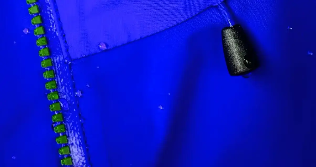 Nahaufnahme einer blauen Gore-Tex-Jacke mit Reißverschluss und Wassertropfen. So pflegt man Gore-Tex richtig beim Waschen.