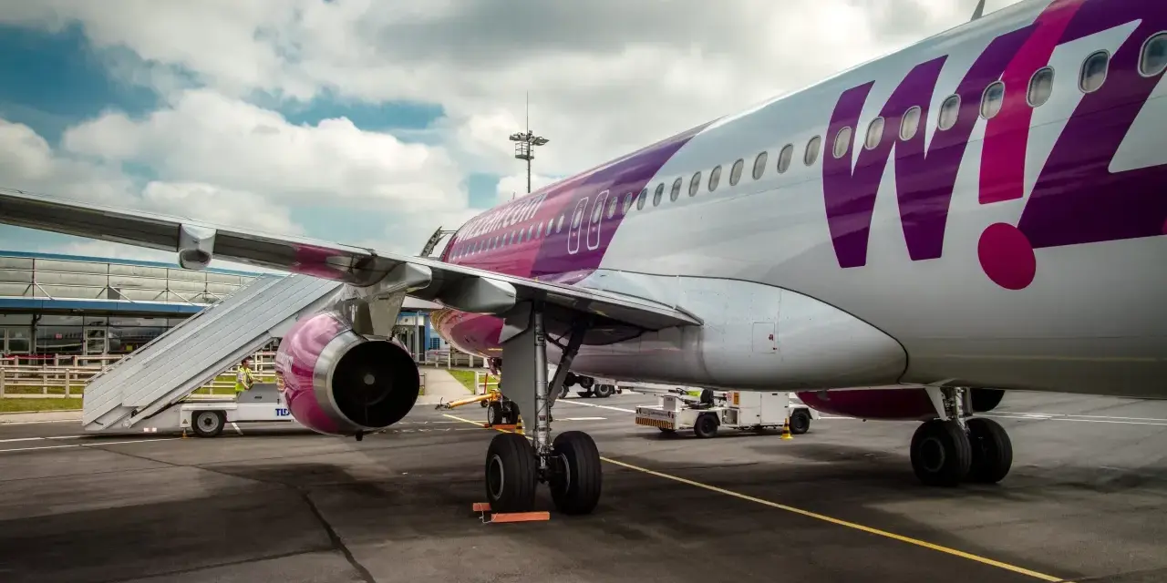 Samolot Wizz Air z fioletowym logo na lotnisku, z drabiną przy skrzydle.