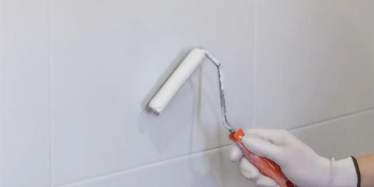 Mano enguantada pintando con rodillo blanco sobre azulejos grises. Renovando el aspecto de los tubos calefacción.