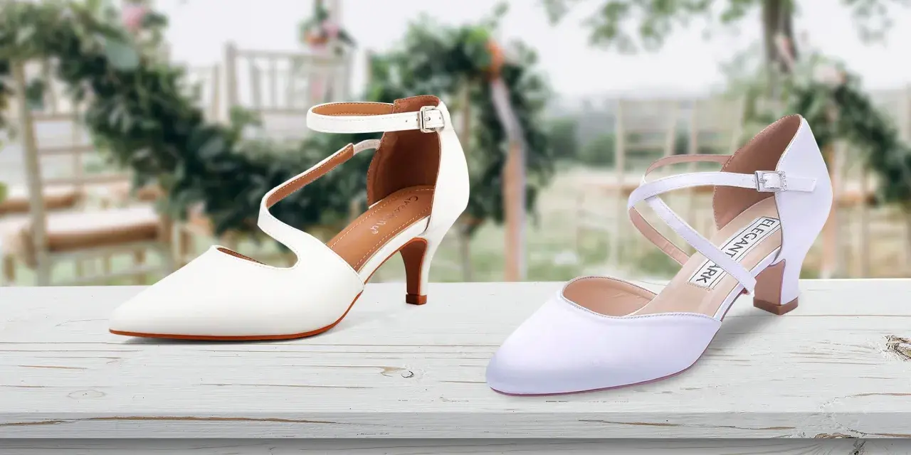 Due eleganti scarpe da sposa bianche, una con cinturino alla caviglia, l'altra con incroci sul collo del piede, su un tavolo di legno con sfondo sfocato di un matrimonio.
