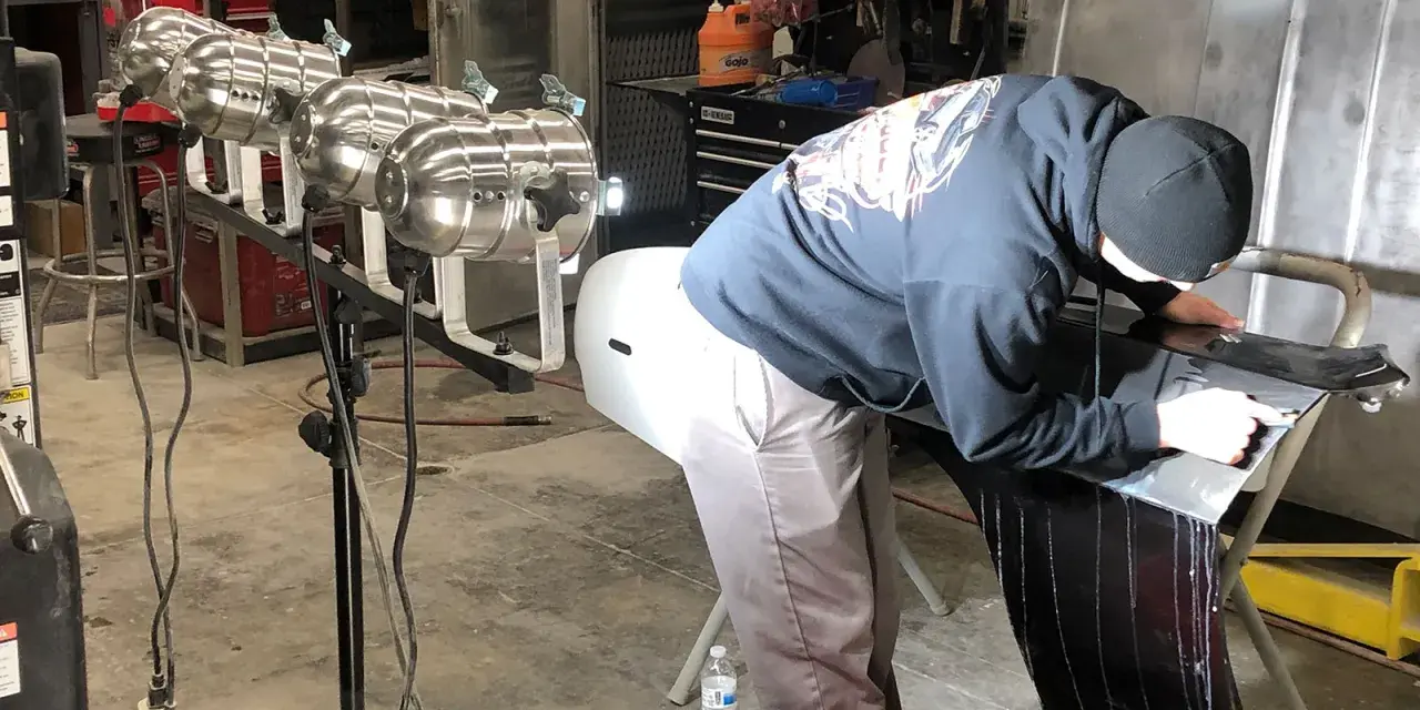 A person in a garage works on a car part, learning how to buff it to a shine.