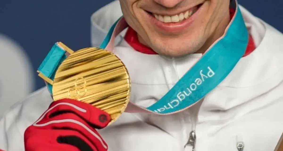 Uśmiechnięty sportowiec w czerwonej rękawicy trzyma złoty medal olimpijski z PyeongChang. Taki medal to marzenie o emeryturze.