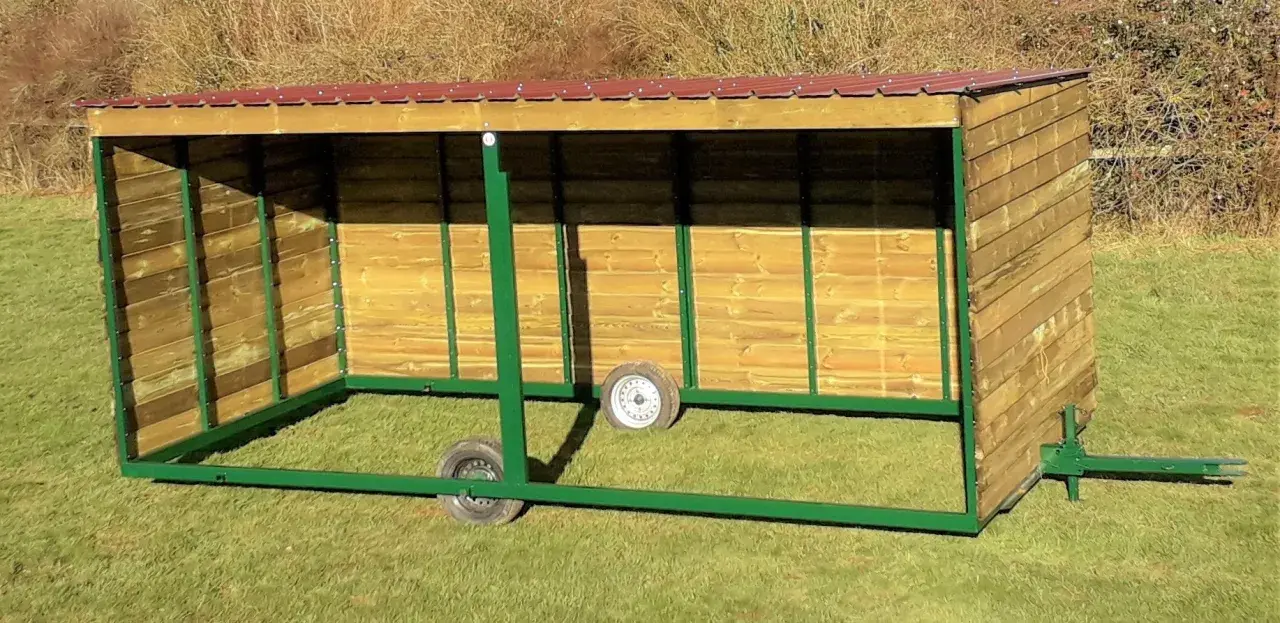 Abri pour chevaux en bois, mobile et sans permis de construire, avec toit rouge et structure verte.
