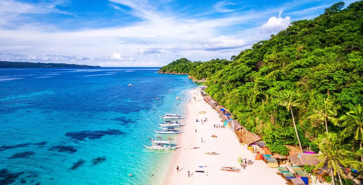 Rajska plaża na Filipinach z turkusową wodą, białym piaskiem, łodziami i zielonymi wzgórzami.