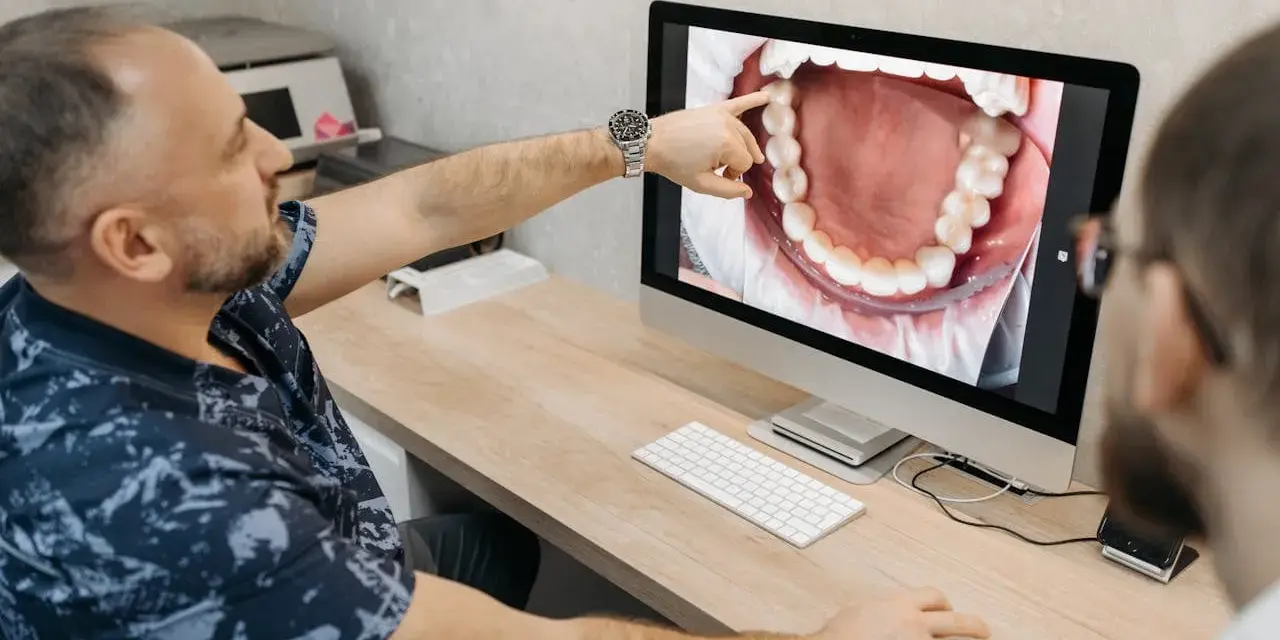 Dentysta omawia z pacjentem czyszczenie kieszonek dziąsłowych, wskazując na ekranie powiększony obraz jamy ustnej.