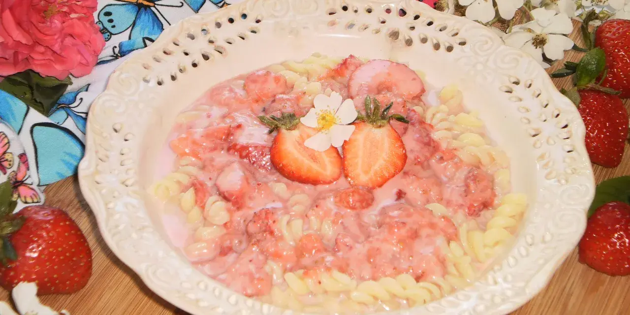 Makaron fusilli z sosem truskawkowym, udekorowany połówkami truskawek i kwiatkiem.