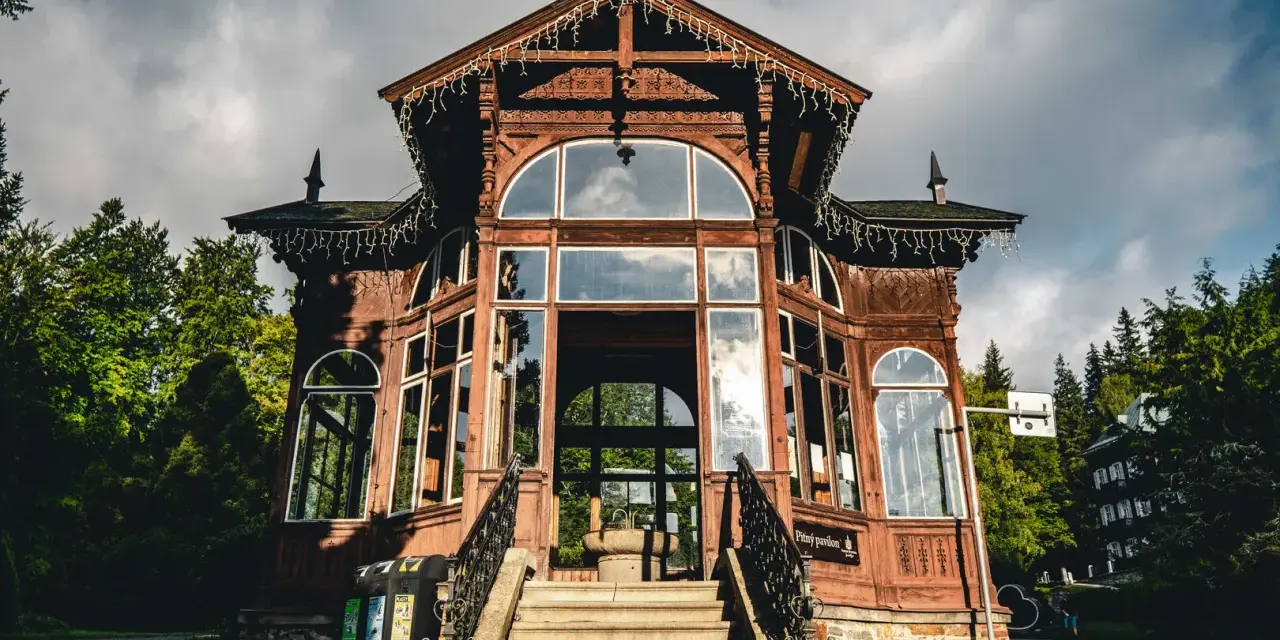 Drewniany pawilon w Karlovej Studance, ozdobiony lampkami, zaprasza do środka. Wspaniała architektura i otoczenie lasu tworzą magiczną atmosferę.