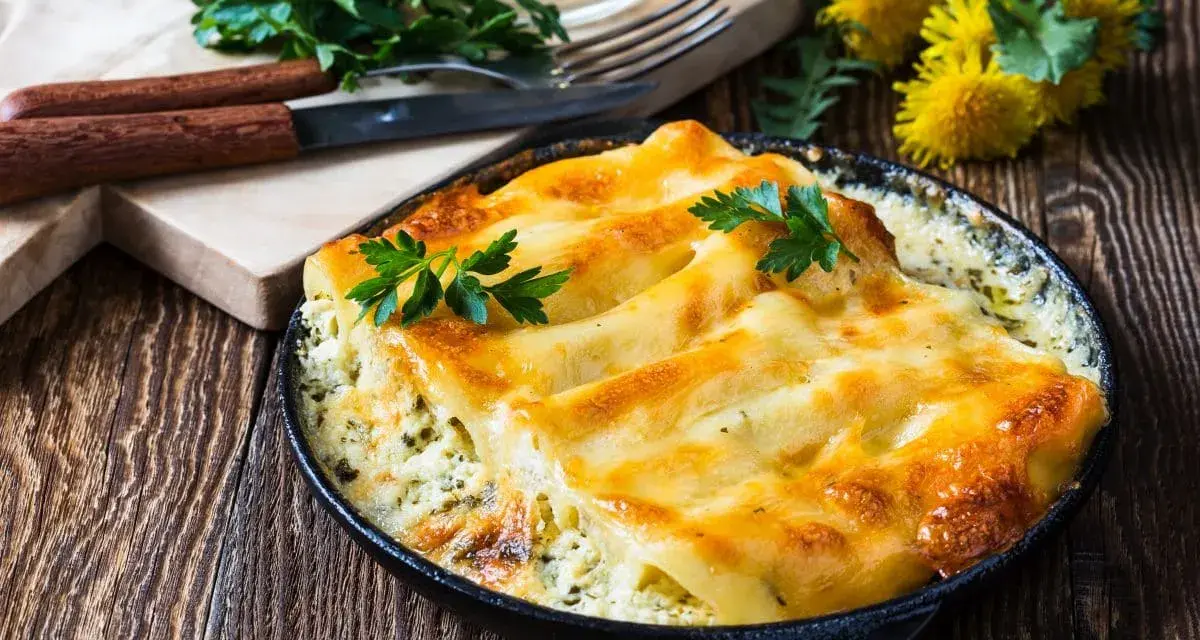 Złociste, zapieczone makaron cannelloni w sosie, udekorowane natką pietruszki, na drewnianym stole.