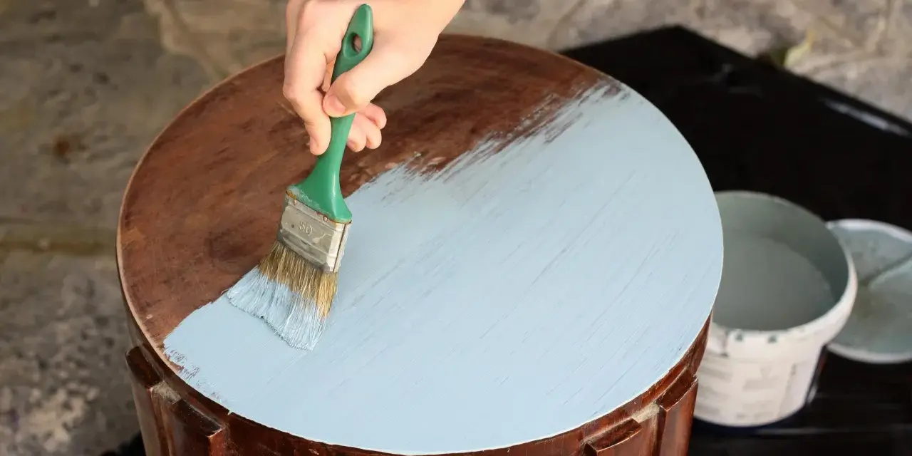 Mano aplicando pintura a la tiza color madera a una mesa redonda.