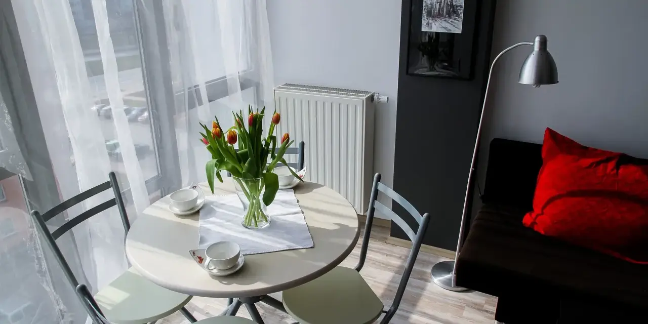 Stół z tulipanami i filiżankami, obok kanapa z czerwoną poduszką. Tak wygląda przytulna garsoniera co to.