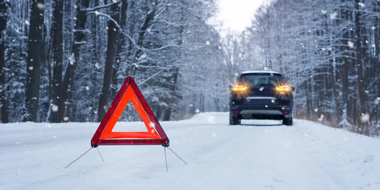 Warnblinkleuchten und Warndreieck auf verschneiter Straße. Ein Auto steht im Hintergrund. Ein wichtiger Hinweis für den auto wintercheck.