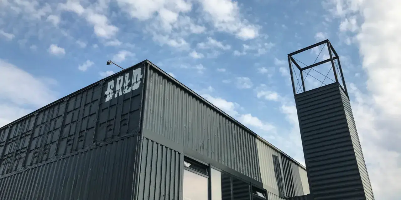 Moderne Containerarchitektur am **brlo gleisdreieck** mit Schriftzug "BALD" und einem markanten Turm unter blauem Himmel.