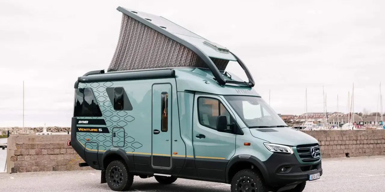 En grön Hymer Venture S husbil med uppfällt tak står parkerad vid en hamn.
