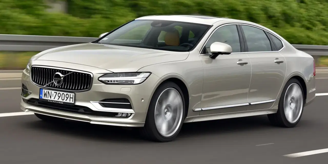 Eleganckie Volvo S90 w kolorze szampańskim pędzi po drodze. Choć piękny, warto pamiętać o potencjalnych wadach tego modelu.