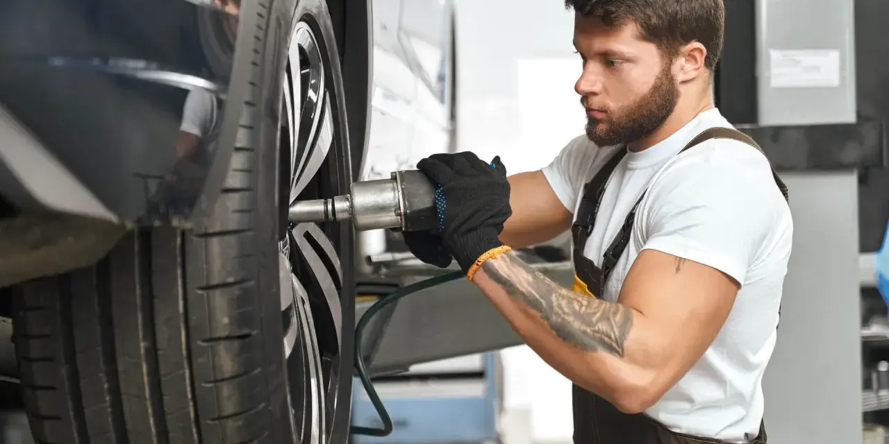 Meccanico con guanti neri lavora su una ruota. Per sapere ogni quanto girare le gomme, consulta il manuale dell'auto.