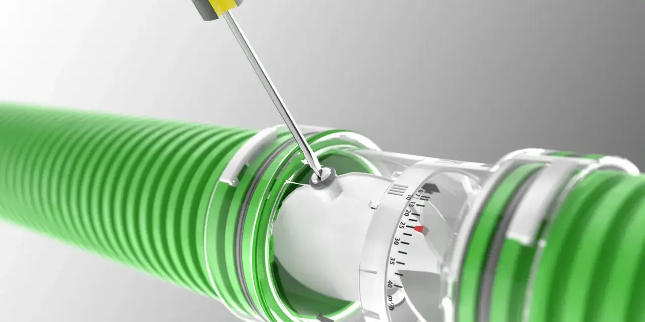 A screwdriver adjusts a clear dial on a green hose, indicating the regulador caudal.