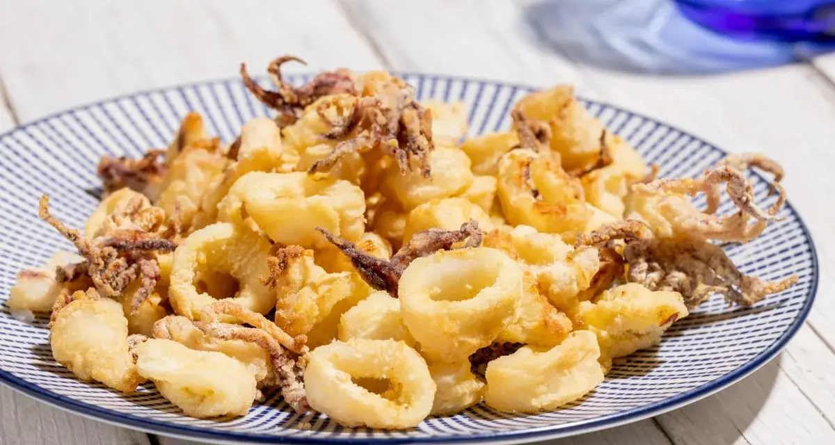 Calamari croccanti e dorati, cotti alla perfezione nella friggitrice ad aria, serviti su un piatto a righe blu.