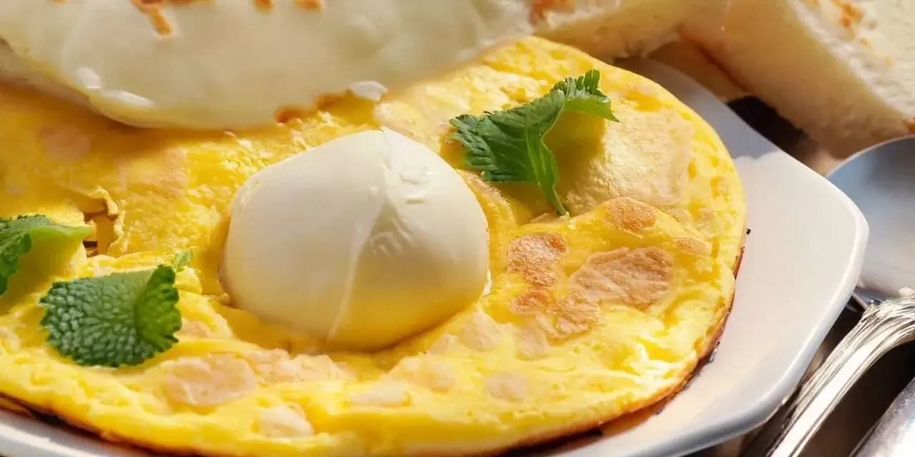 Frittata soffice con mozzarella filante, guarnita con foglie di menta fresca. Accompagnata da fette di pane tostato.