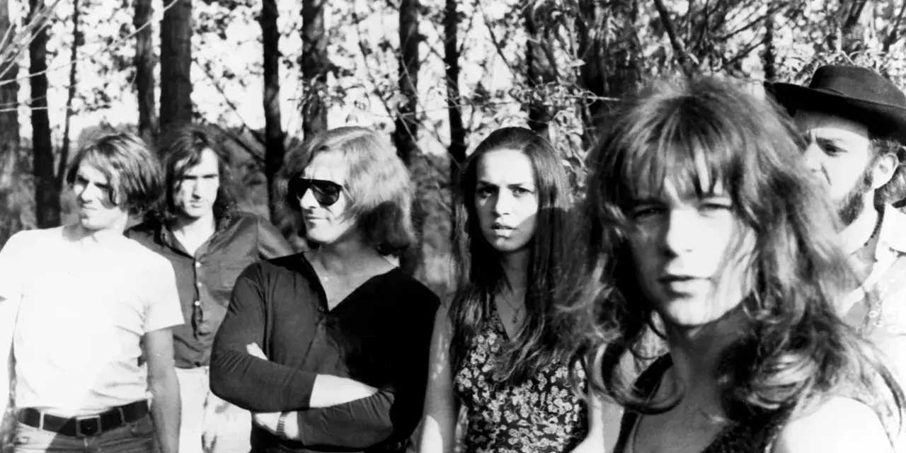 Un groupe rock allemand des années 70, avec des membres aux cheveux longs et des tenues décontractées, posant devant des arbres.